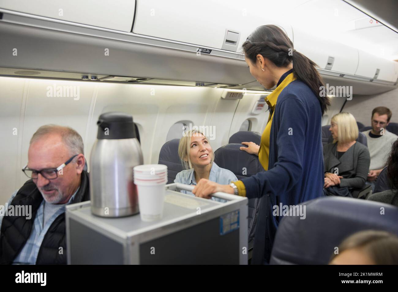 Flight attendant with beverage cart talking to passenger in airplane