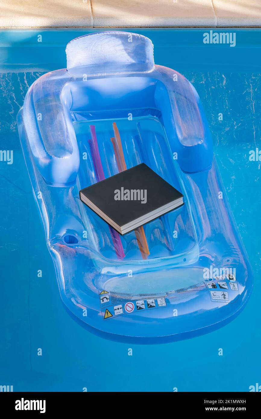 A black book rests on an inflatable pool mat floating on the water Stock Photo