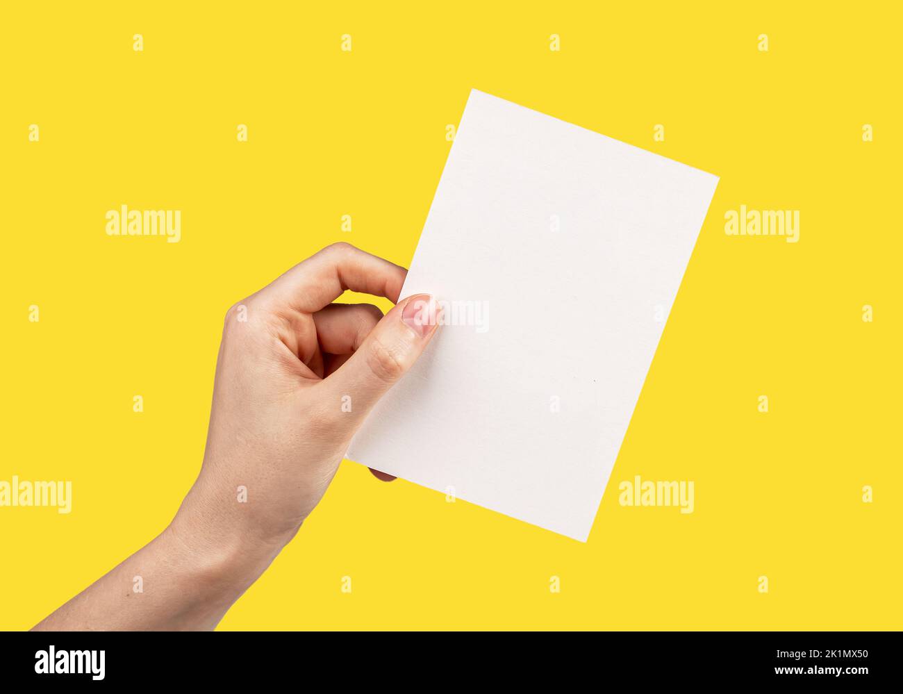 Hand holding greeting card mockup on yellow background. White empty paper for text. Invitation, letter, gift, certificate template. High quality photo Stock Photo