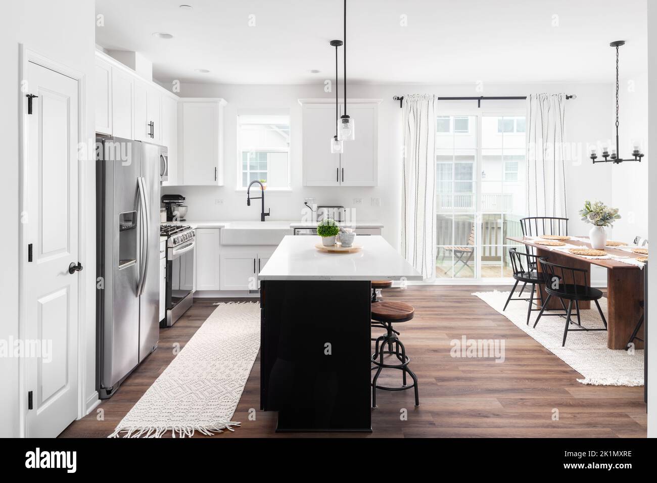 A modern farmhouse kitchen and dining rom with a black island, white ...