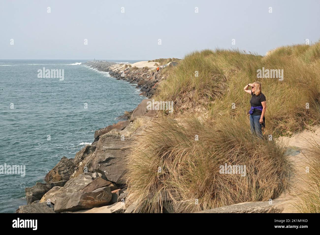 A woman stands on the rocky jetty leading into the Pacific Ocean in Florence, Oregon. Stock Photo