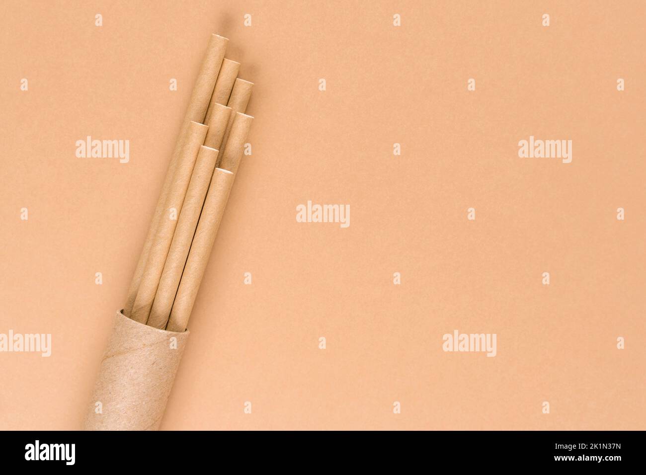 Paper drinking straws in packaging paper tube over light brown