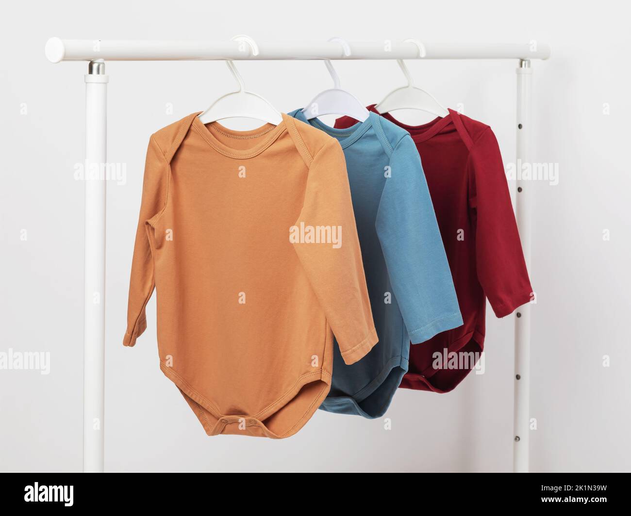 Multicolored long sleeve baby bodysuits hanging on a hanger Stock Photo