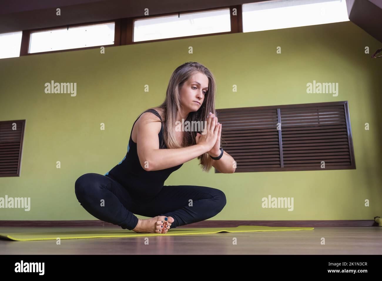 A woman in sportswear practicing yoga, performs a variation of the exercise Baddha konasana, butterfly pose, trains in a room on a mat Stock Photo