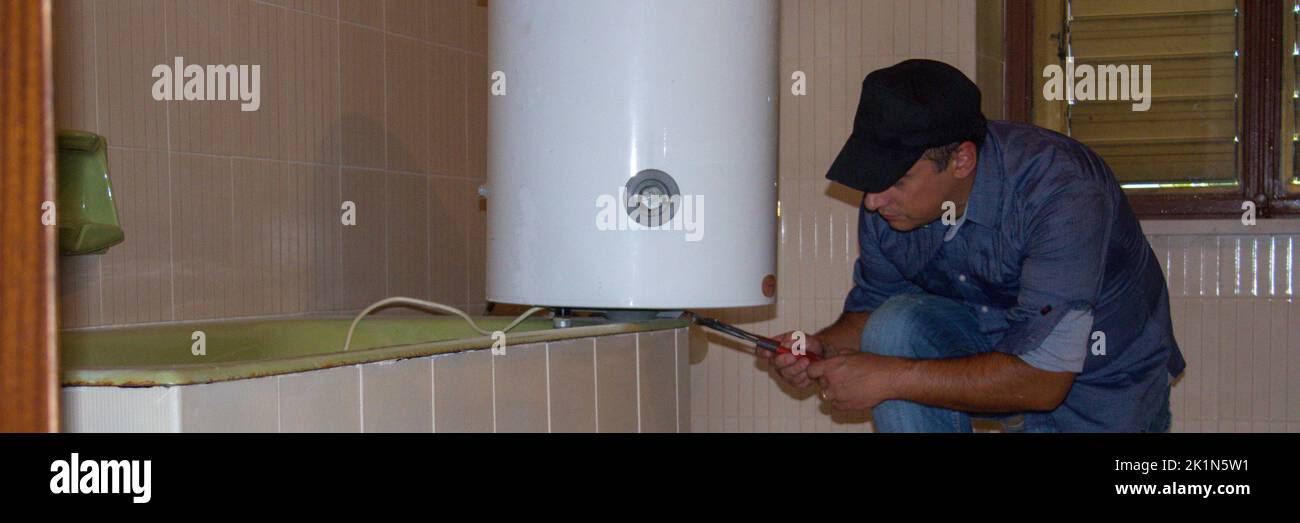 Plumber in the bathroom at home while repairing a water heater. Plumbing and DIY work. Horizontal banner Stock Photo