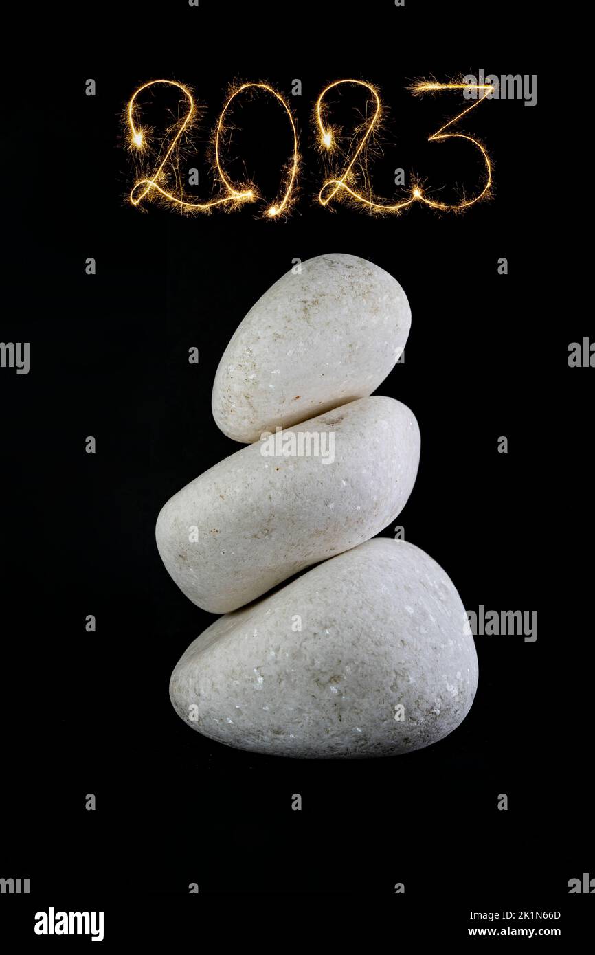 3 white stones stacked, isolated on black background with 2023 new year written above with fireworks sparks Stock Photo