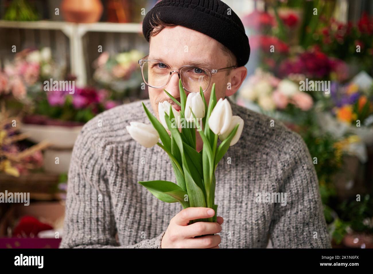 Bearded florist hipster caucasian male in sweater sniffing beautiful bouquet of spring white tulip bouquet. Mother's Day, dating, love, romantic or International Women's Day concept Stock Photo