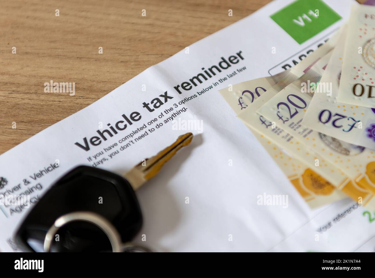 A vehicle tax reminder document of a desk with car keys and money. Stock Photo