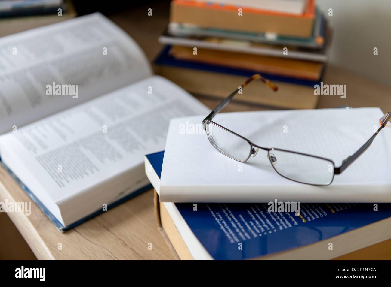 A pair of glasses and on a pile of printed books on a desk. Stock Photo