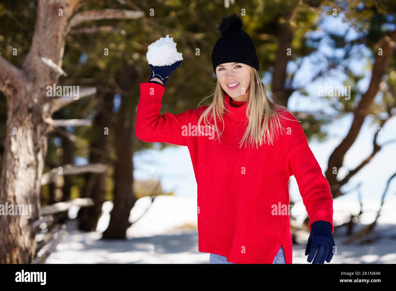 Blonde woman throwing snowballs forward in a snow-covered forest in the mountains Stock Photo
