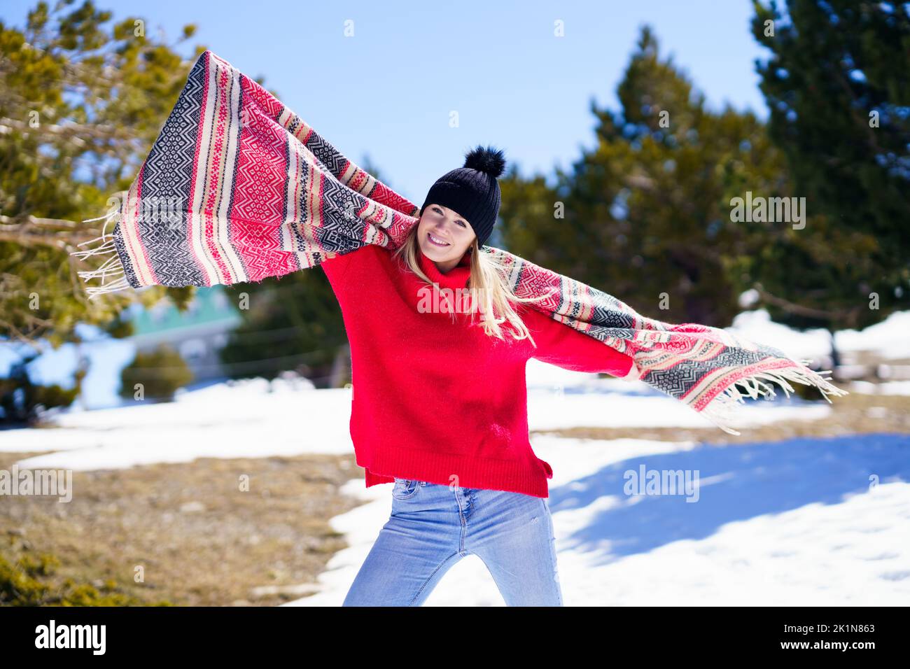 Happy young blonde woman waving her scarf in the wind in a forest in the snowy mountains. Stock Photo