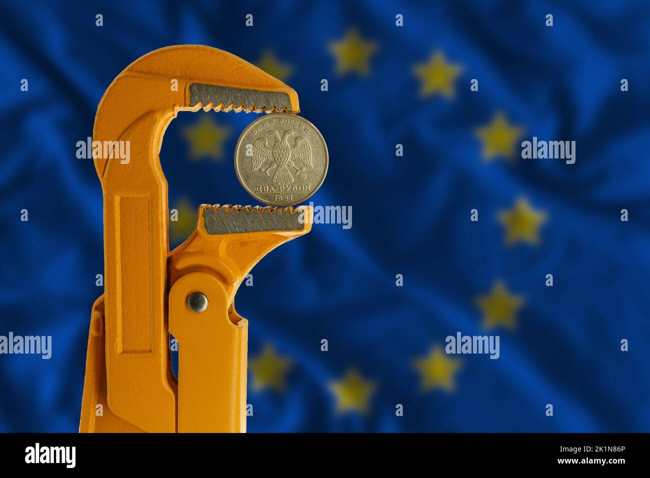 Russian two rubles coin clamped in an orange plumber wrench on the background of the European Flag. obverse side coin Stock Photo