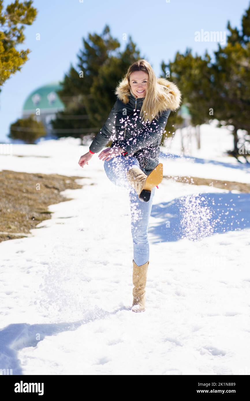 Blonde happy woman kicking snow in a snow-covered forest in the mountains Stock Photo