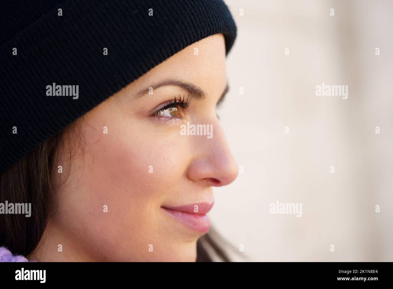 Closed portrait of young woman leaning against a wall outdoors with eyes of hope and joy. Stock Photo