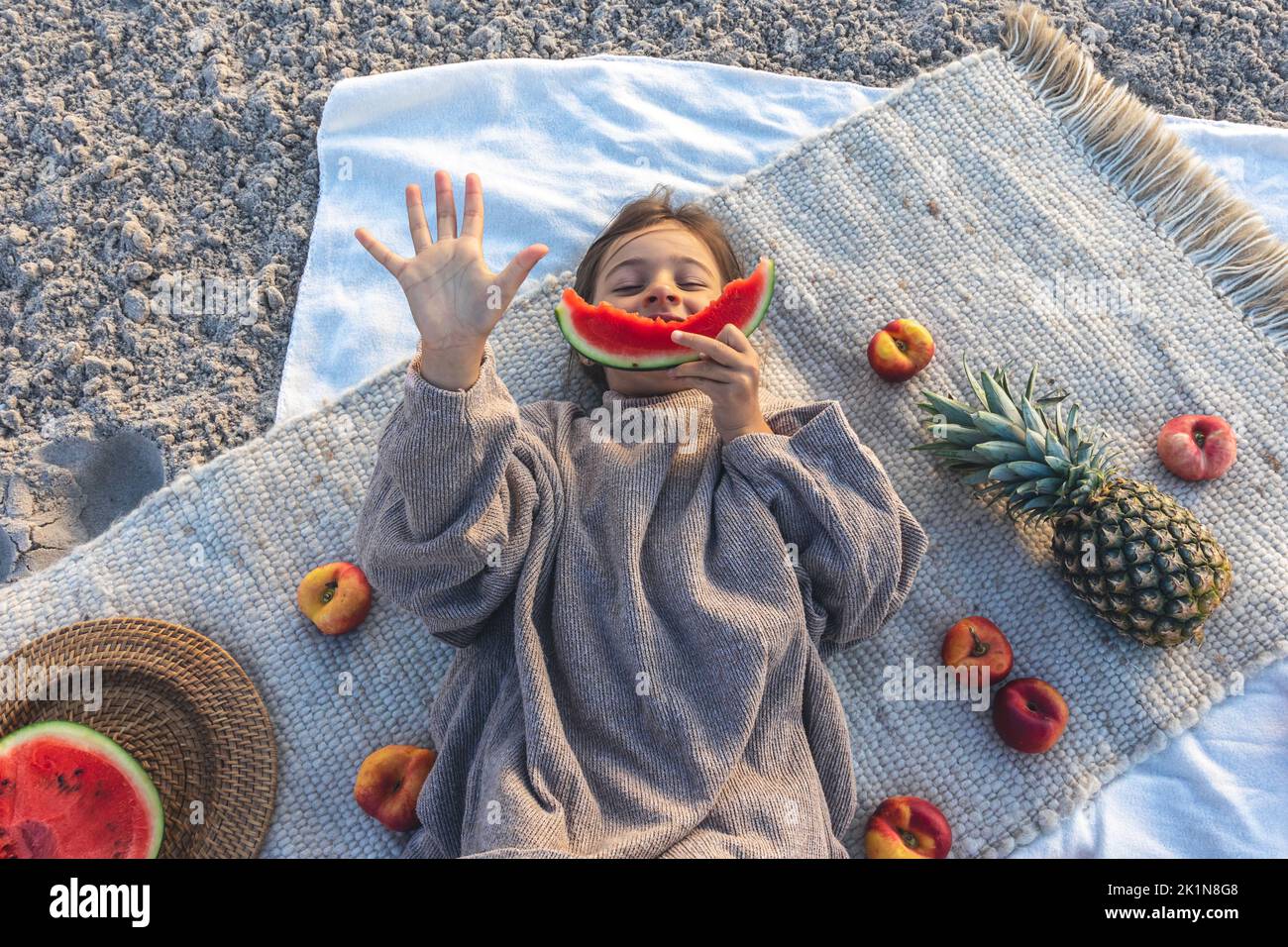 Little girl eats fruit lying on a blanket on the beach Stock Photo Alamy