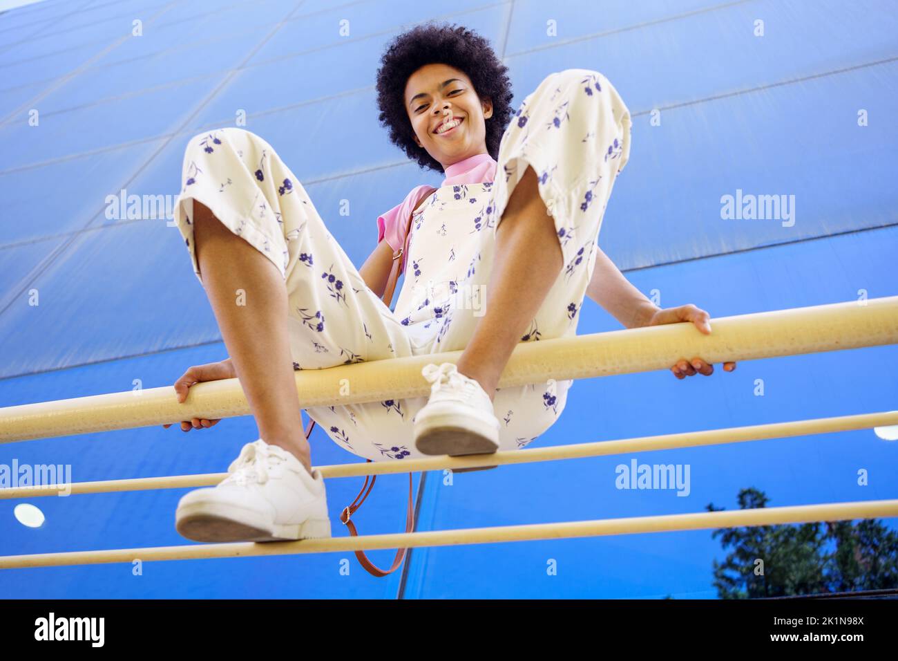 Smiling black woman sitting on fence in city Stock Photo