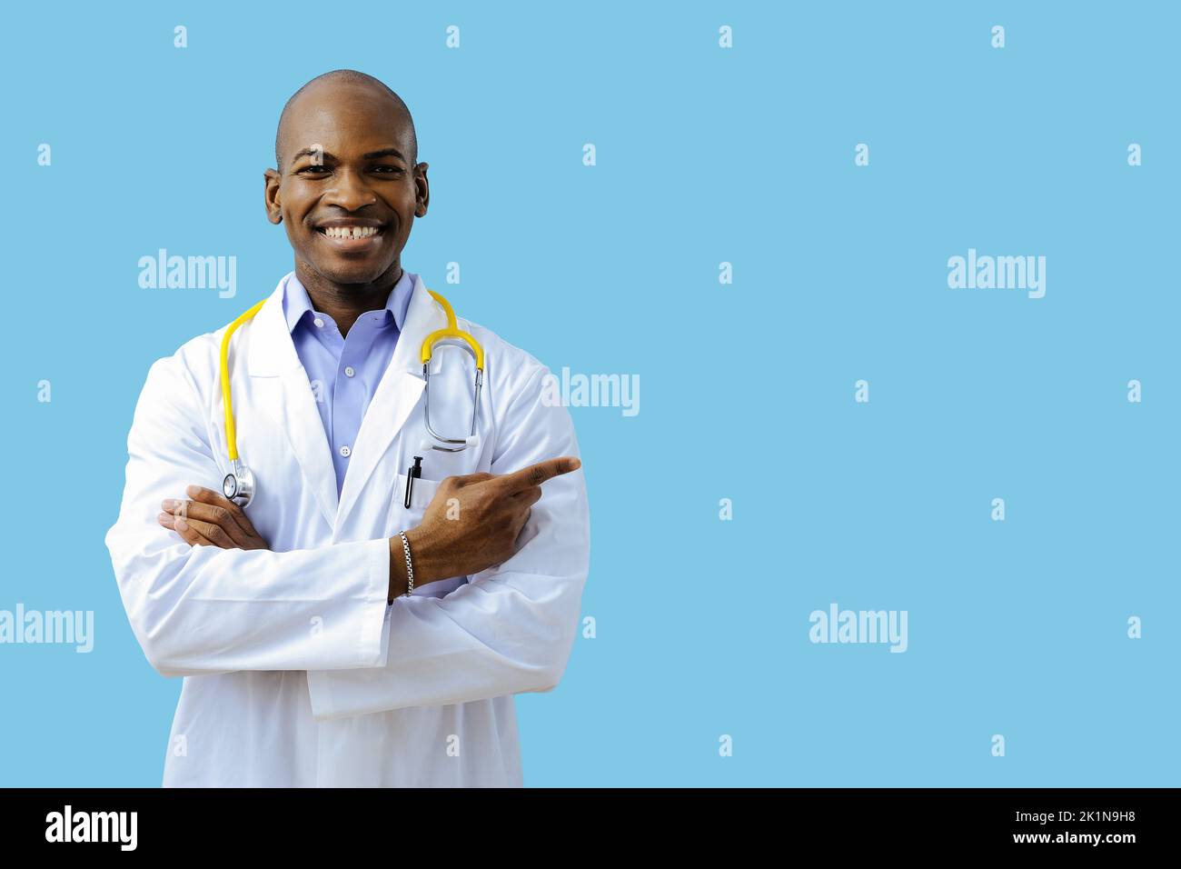 Doctor with folded arms wearing lab coat pointing at copy space indoors studio Stock Photo