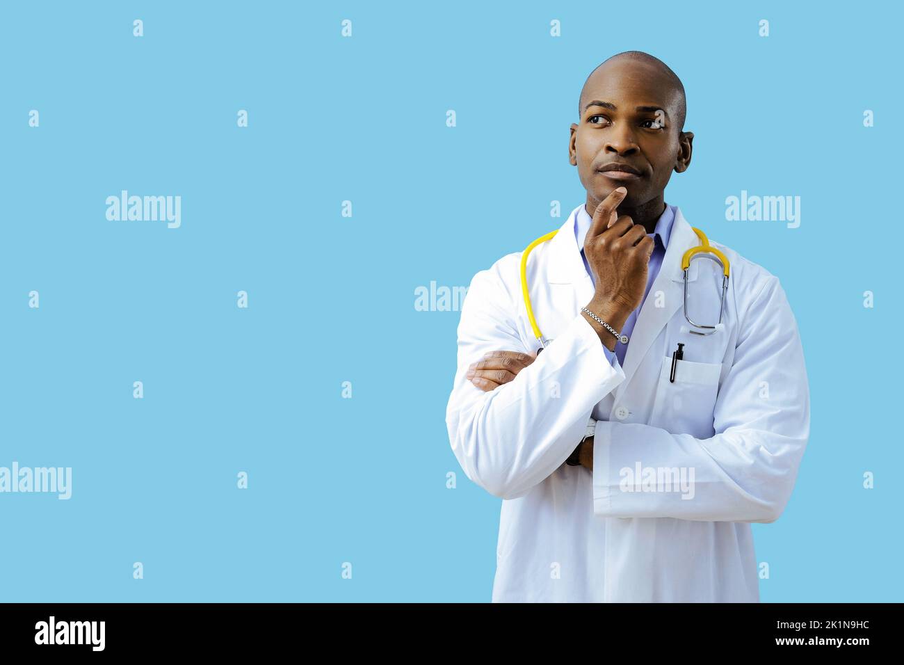 Thoughtful doctor with folded arms hand on chin wearing lab coat looking up at copy space indoors studio Stock Photo