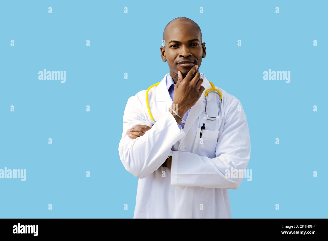 Thoughtful doctor with folded arms hand on chin wearing lab coat indoors studio Stock Photo