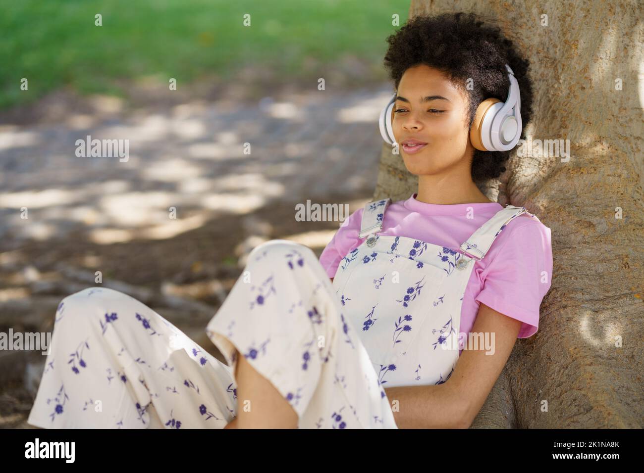 Content black woman listening to music near tree Stock Photo
