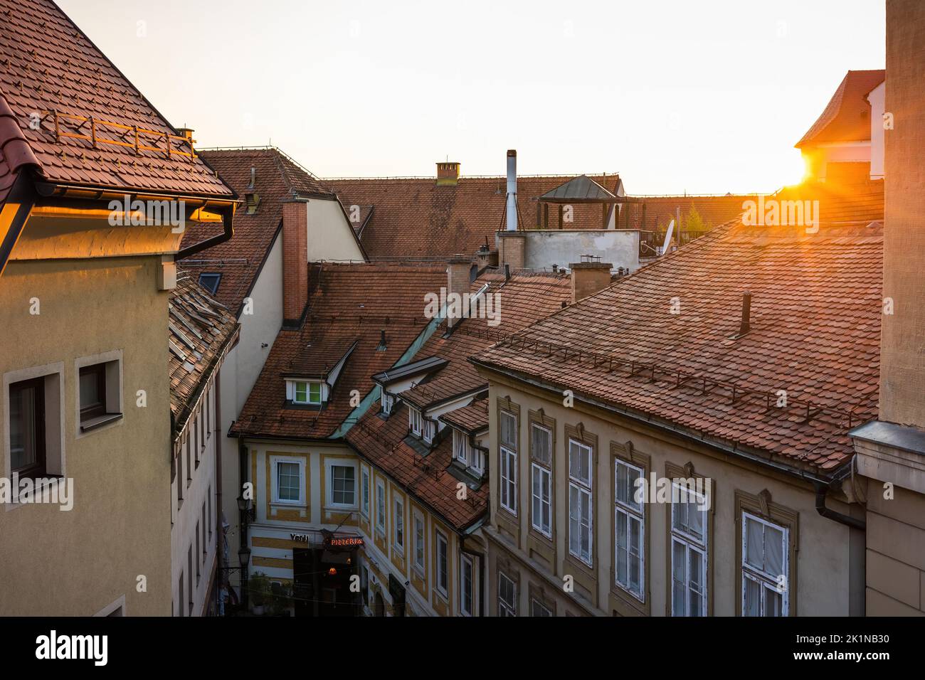 Sun setting over rooftops with red tiles in a city with old houses Stock Photo
