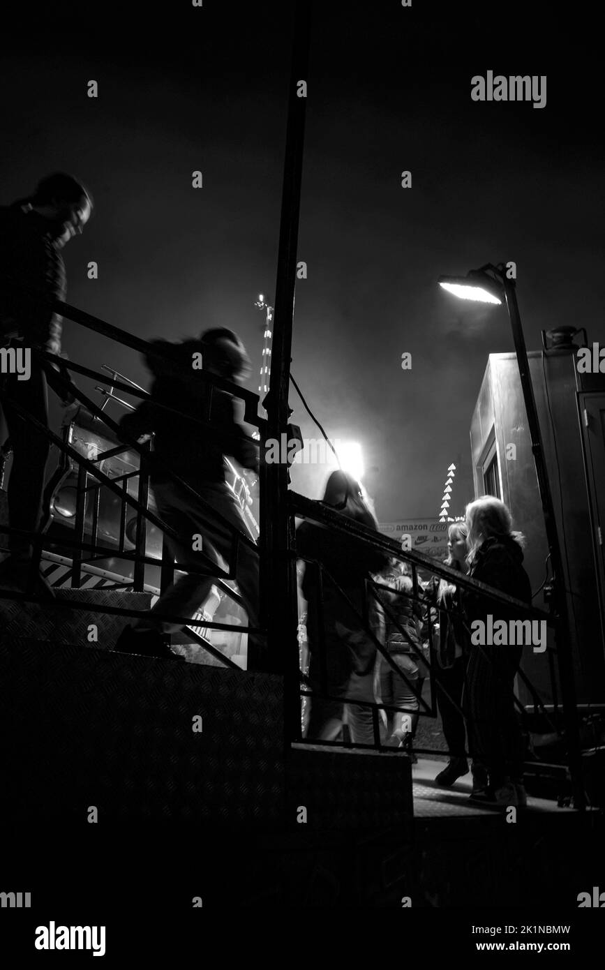 Teenagers walking down steps off an amusement ride at night, Funfair UK Stock Photo