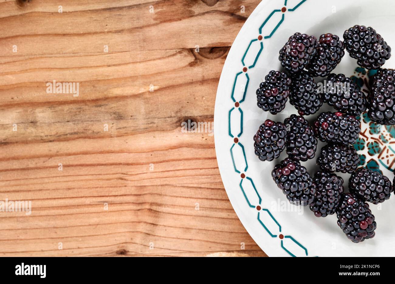Fresh wild blackberries on white plate on wooden table , edible fruit Stock Photo