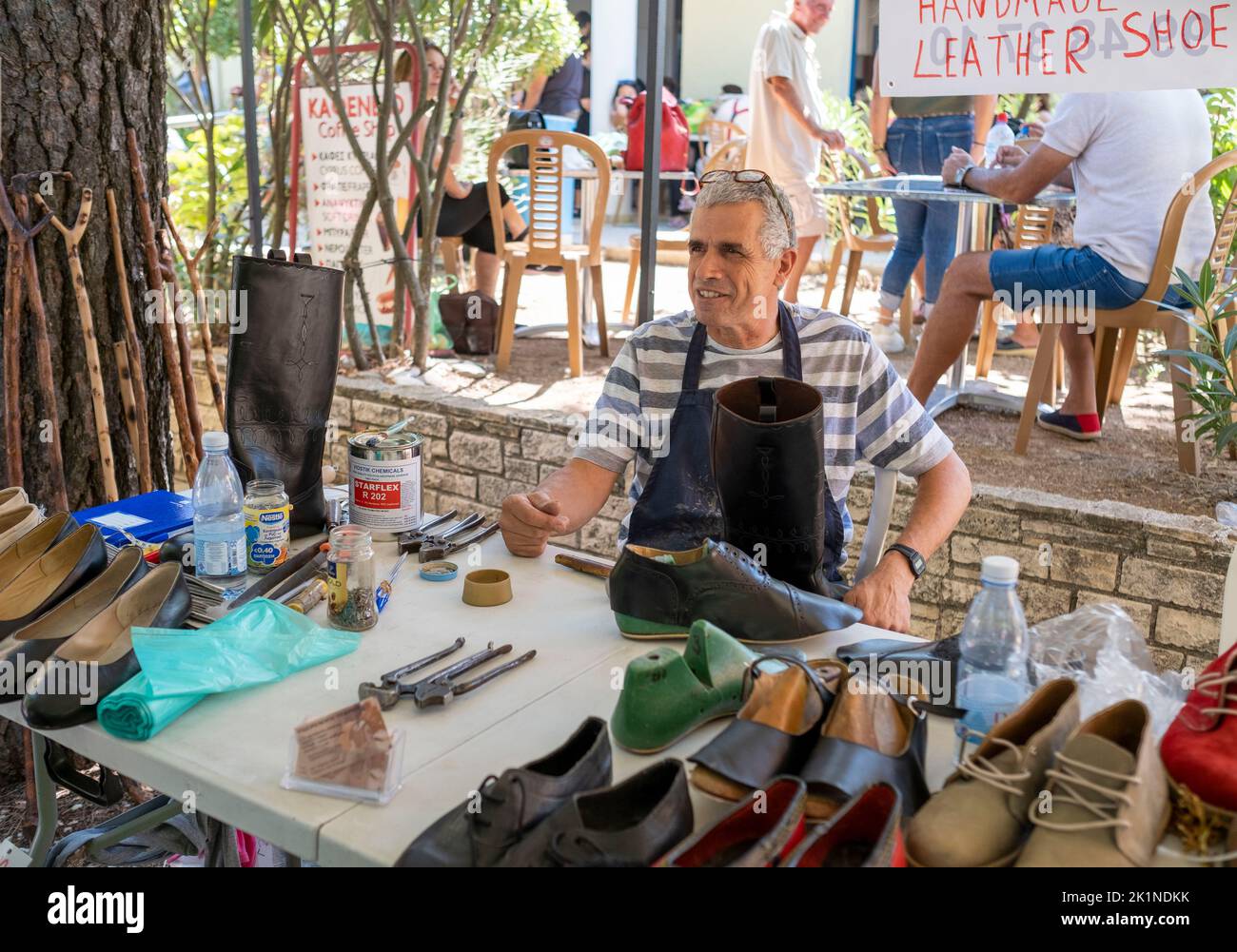 A cobbler speaks with customers at his stall during the Statos-Ayios Fotios Rural Festival. Paphos region, Cyprus Stock Photo