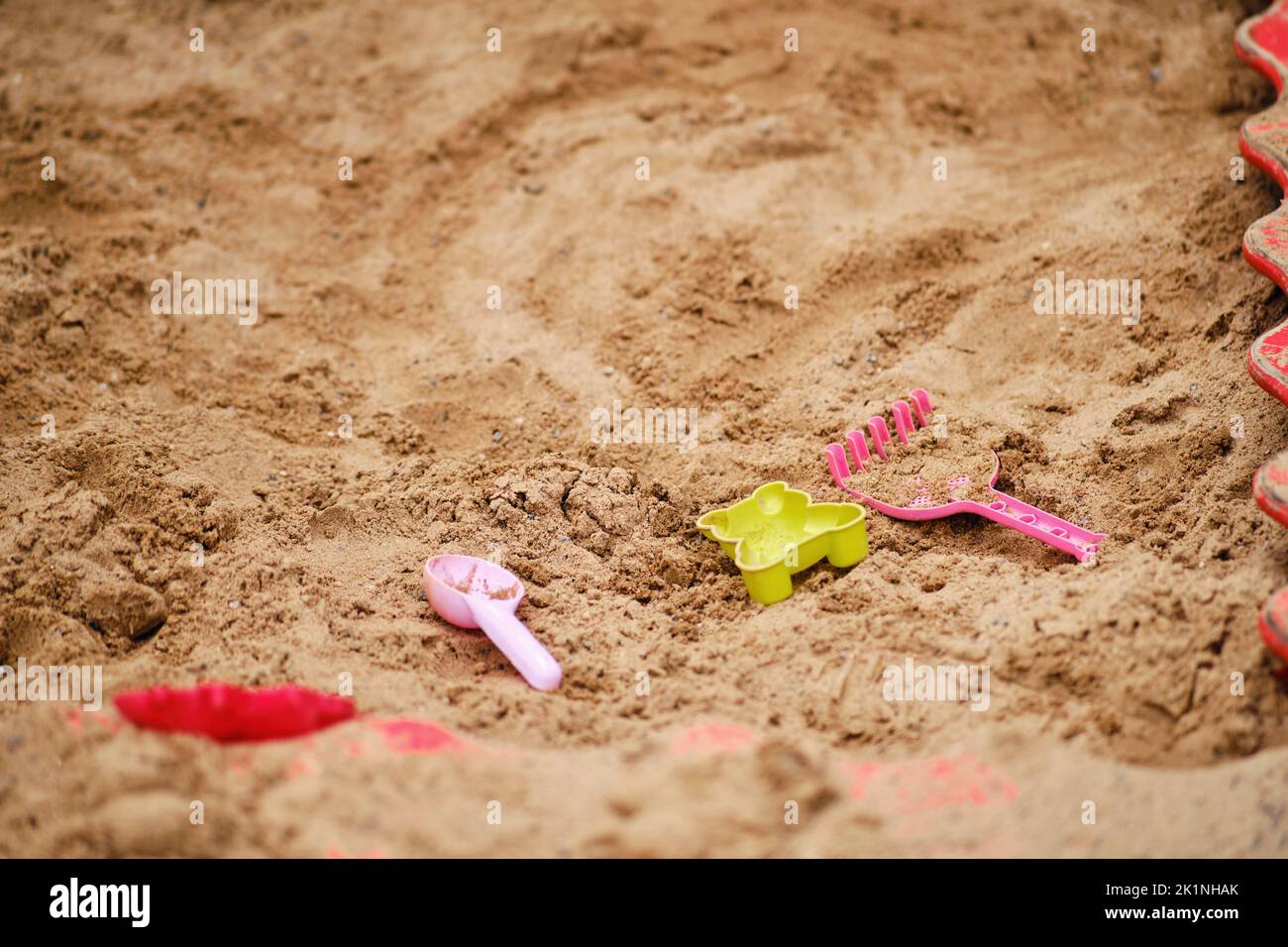 Children toys lie forgotten in an empty sandbox. A shovel, a rake and a sand mold are lying on the playground, there are no people Stock Photo