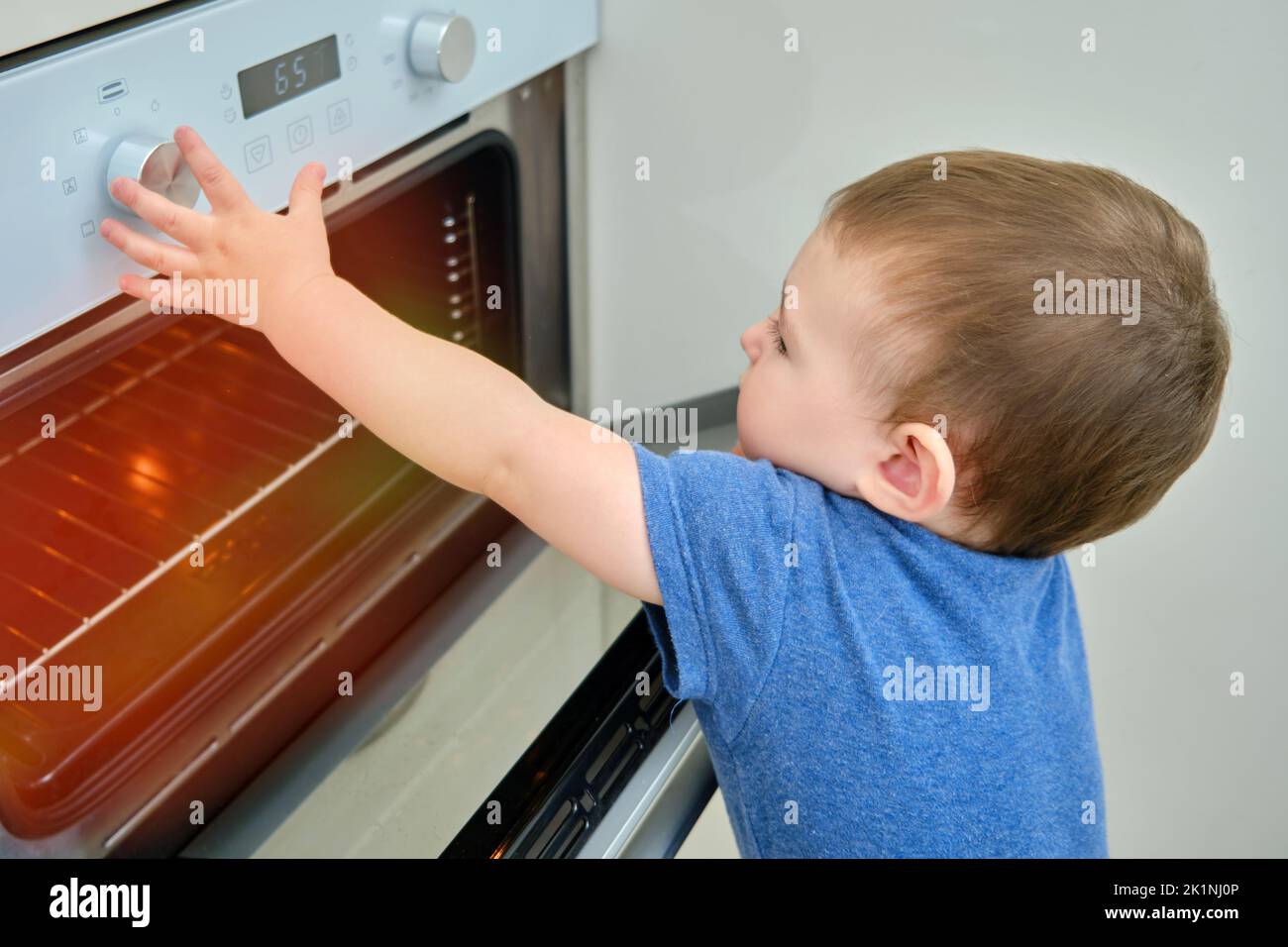 Toddler baby climbs into a hot electric oven. Child boy opens oven door