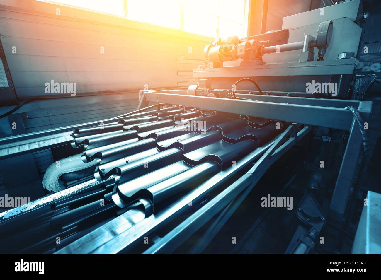 Metal sheet forming machine. Abstract industrial background in blue color. Metal factory, production of roof tile from steel. Stock Photo