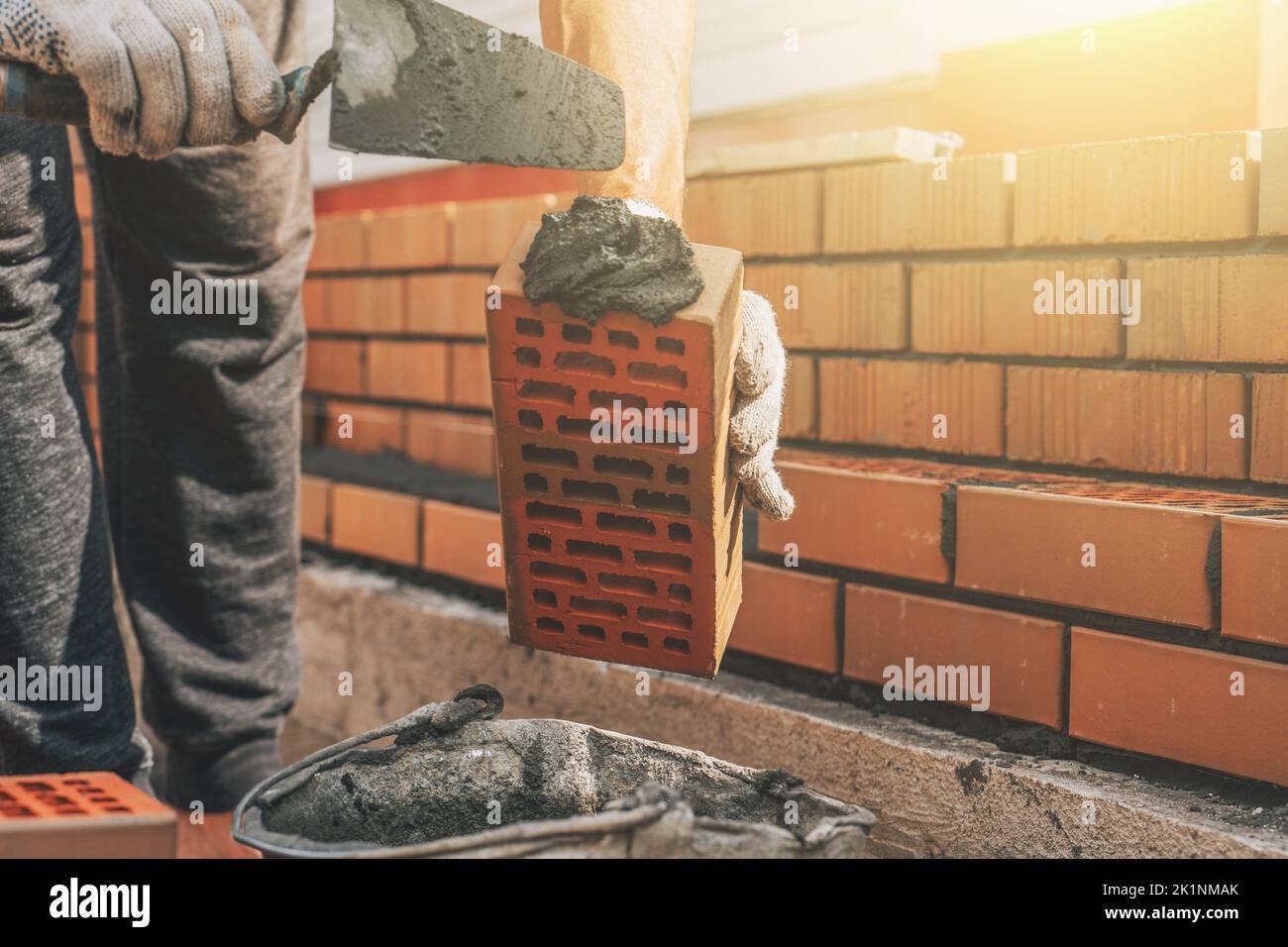 Worker at construction site applies cement mortar to brick for construction of brick house. Stock Photo