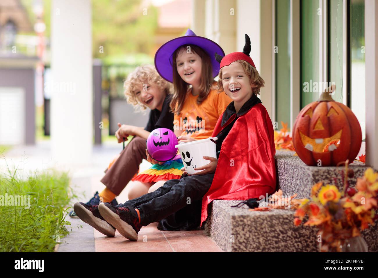 Kids trick or treat on Halloween night. Child at decorated house door. Boy and girl in witch and vampire costume and hat with candy bucket and pumpkin Stock Photo
