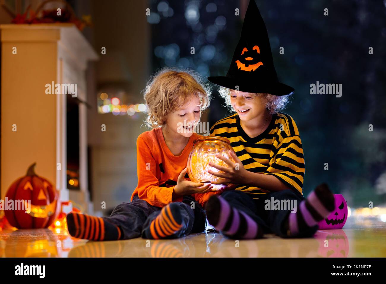 Little girl and boy in witch costume on Halloween trick or treat. Kids holding candy in pumpkin lantern bucket. Children celebrate Halloween at decora Stock Photo
