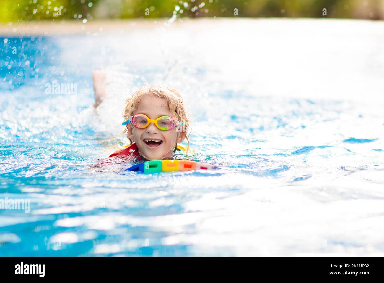 Child learning to swim in outdoor pool of tropical resort. Kids learn swimming. Exercise and training for young children. Little boy with colorful flo Stock Photo