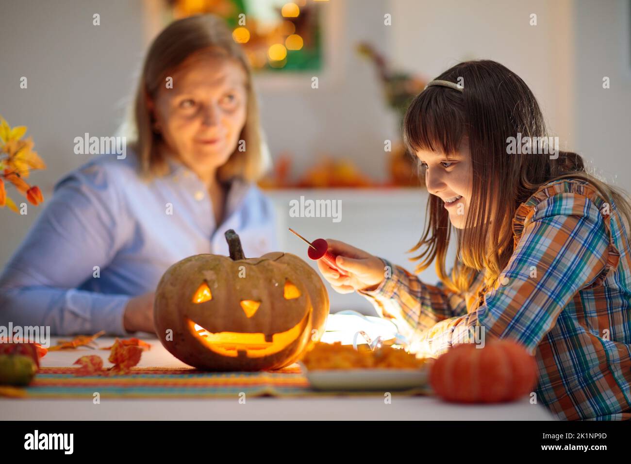 Family carving pumpkin for Halloween celebration. Woman and little girl cutting jack o lantern for traditional trick or treat decoration. Mother and c Stock Photo