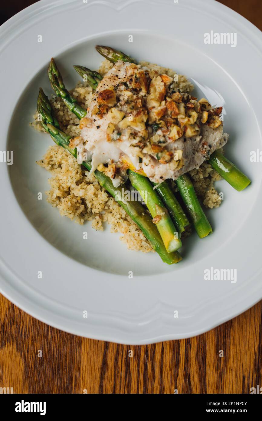 serving of Trout amandine with bulgur wheat and asparagus in white bowl Stock Photo
