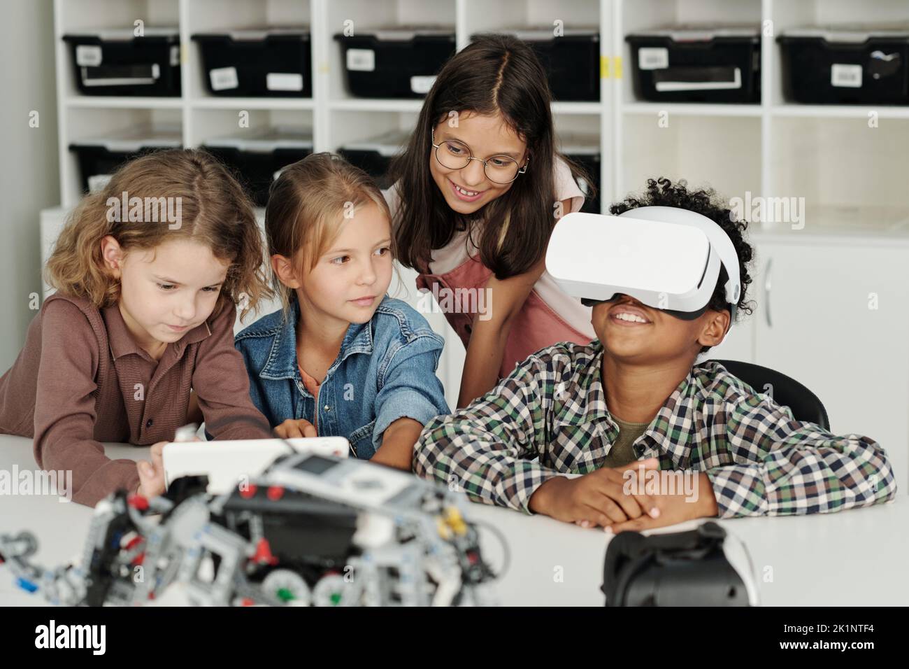 Group of clever schoolchildren stting by desk while one of them making presentation of virtual toys and games to his classmates Stock Photo