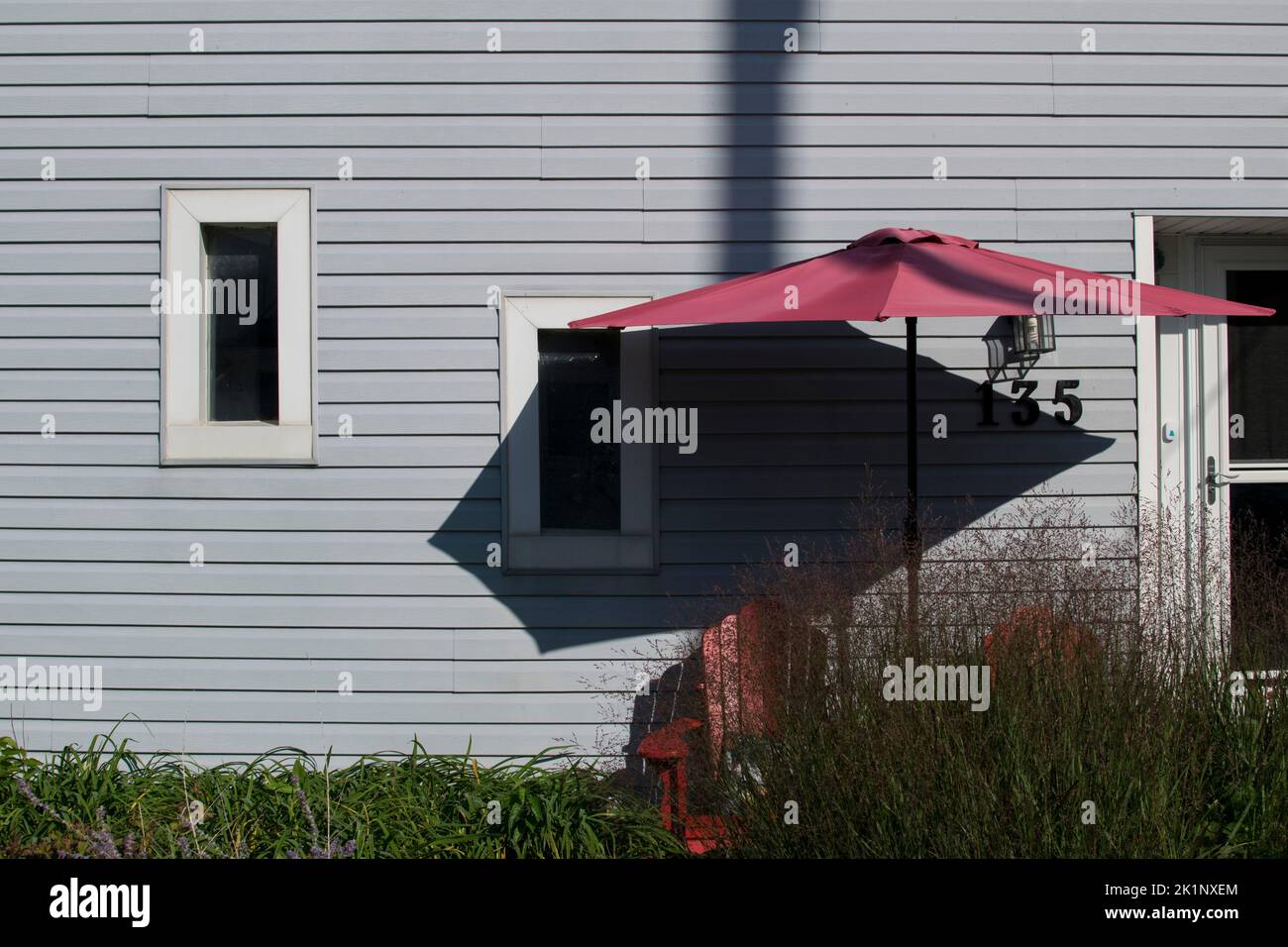 a red chair and umbrella on a porch next to a summer cottage Stock Photo