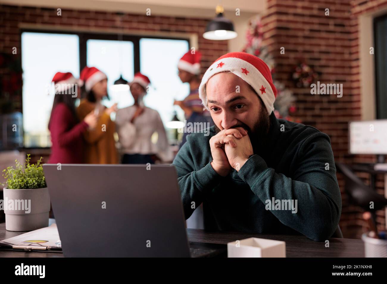 Businessman feeling disturbed at office job because of noisy coworkers celebrating christmas eve. Tired irritated employee being overwhelmed and working during winter holiday season. Stock Photo