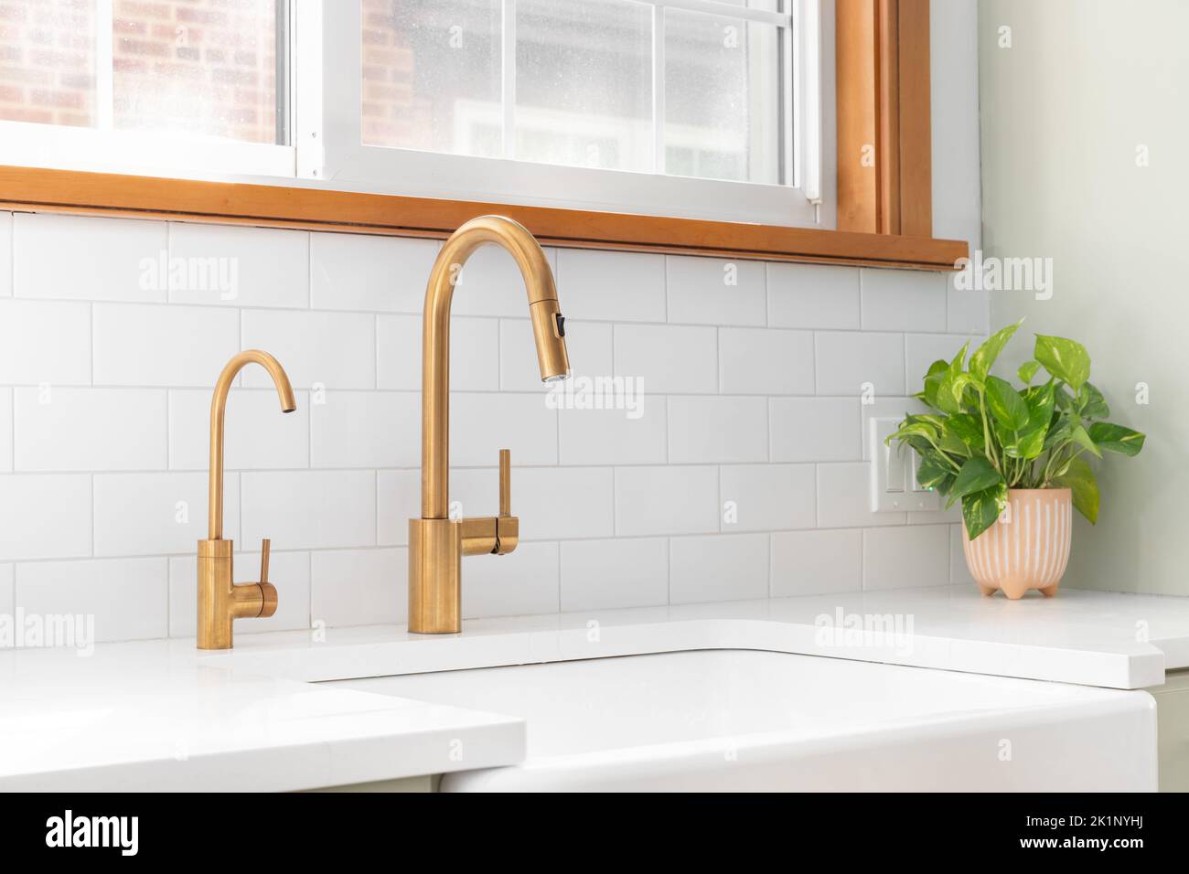 A kitchen sink detail shot with a gold faucet, apron sink, subway tile
