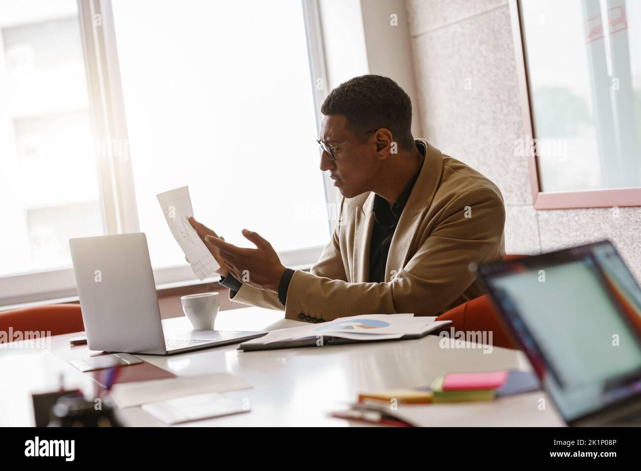 Busy african businessman in glasses working with documents while sitting in modern coworking Stock Photo