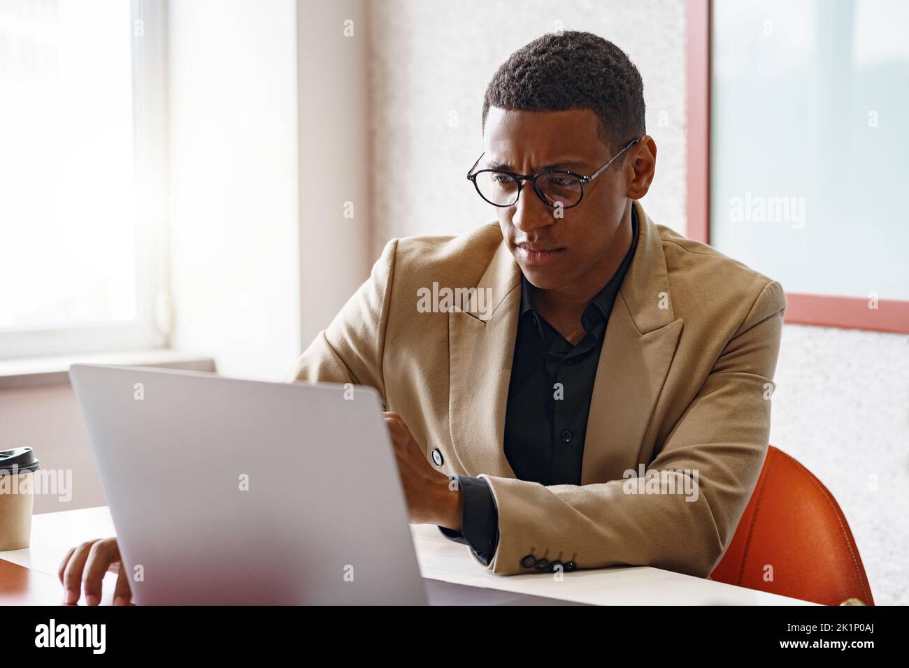 Busy african businessman in glasses working on laptop while sitting in modern coworking Stock Photo