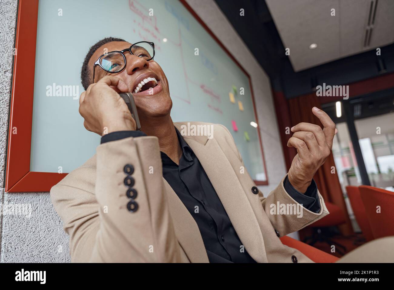 Smiling african businessman talking phone sitting in cozy coworking Stock Photo