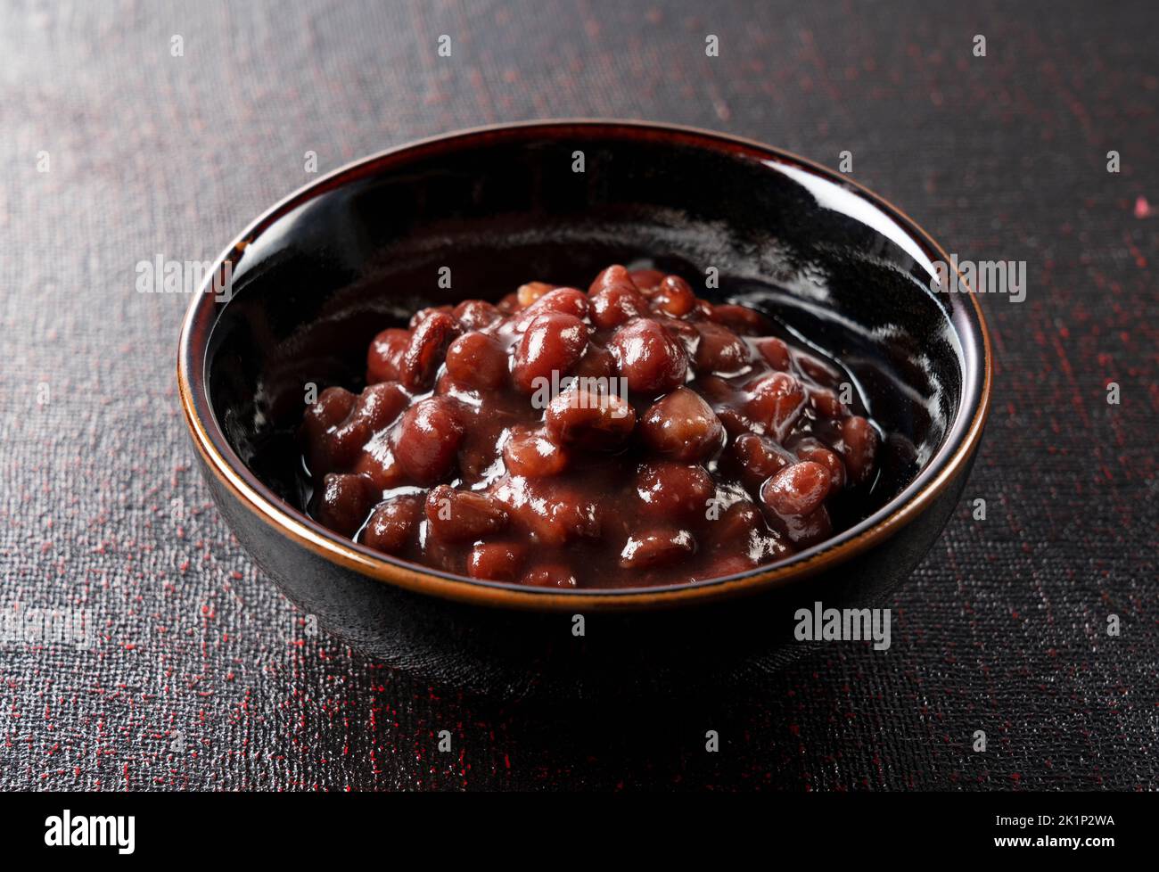 Boiled azuki beans in a small black bowl placed against a black background. Stock Photo