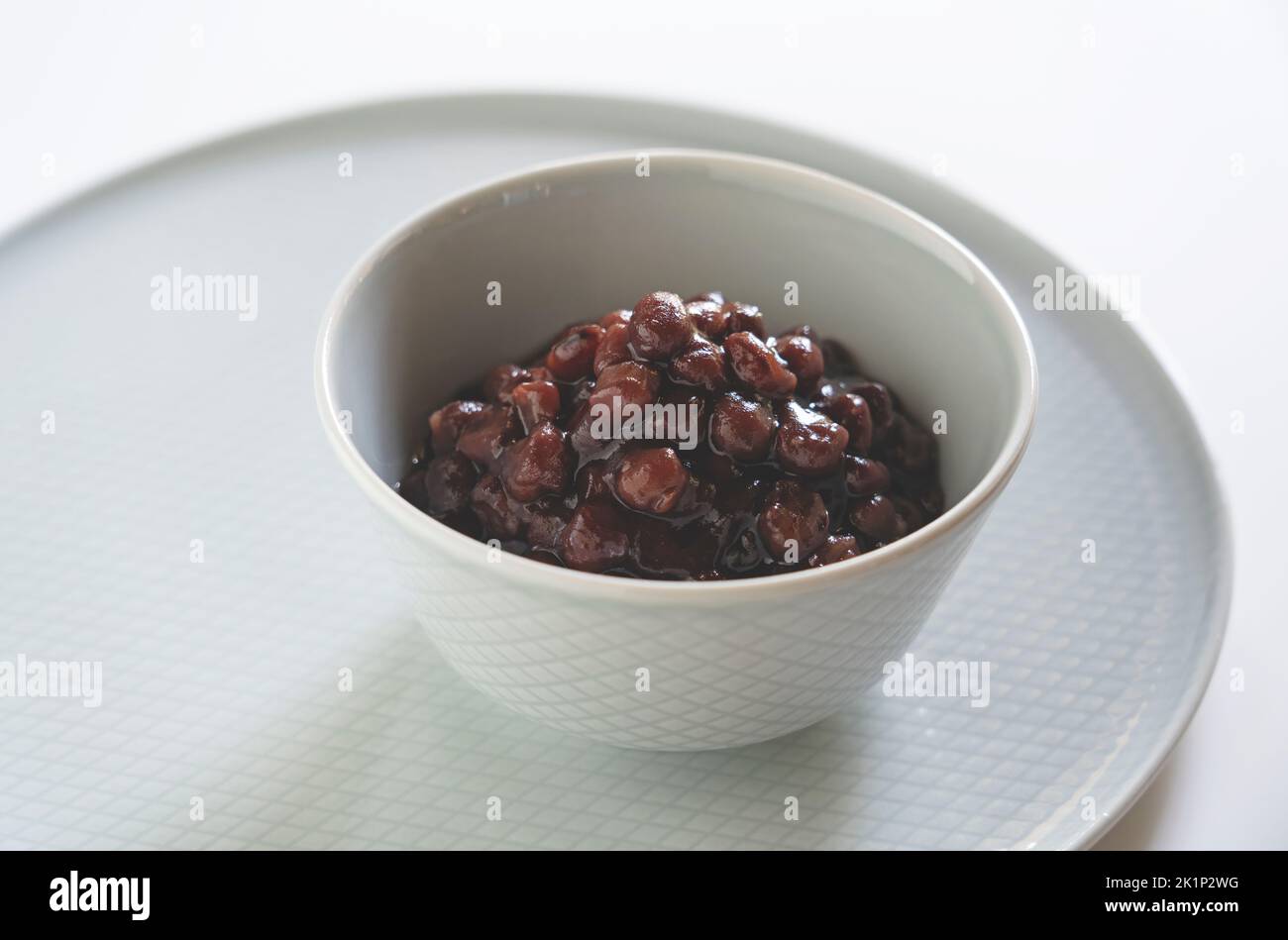 Boiled azuki beans in a small bowl placed against a white background. Stock Photo