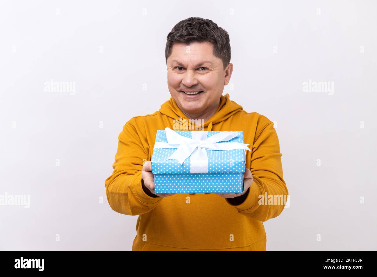 Portrait of positive generous man smiling and giving gift box, sharing holiday present, charity concept, wearing urban style hoodie. Indoor studio shot isolated on white background. Stock Photo