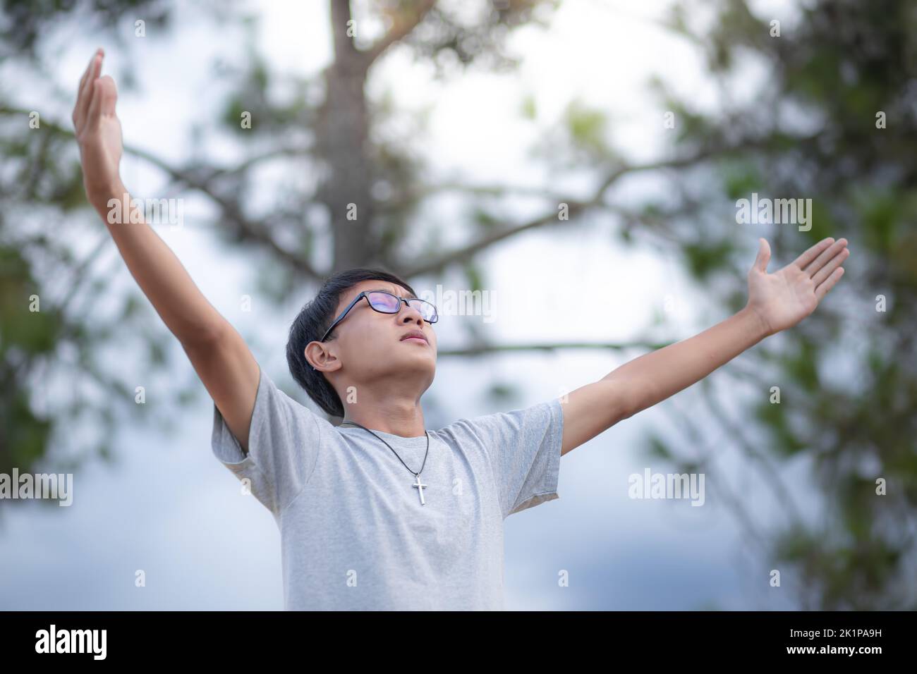 Young man lift hands up and prayer near a tree. concept religion. focus ...