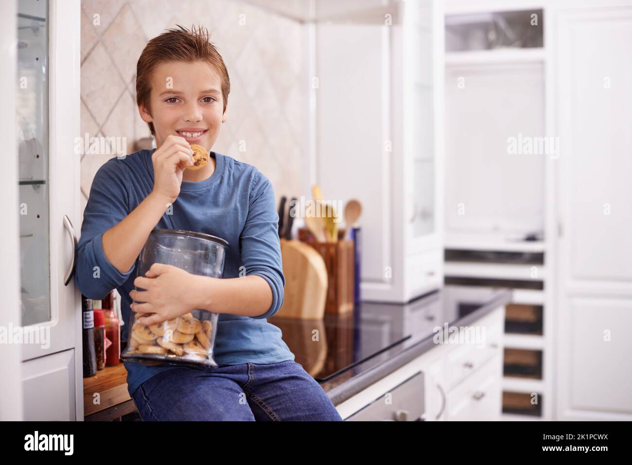 One more wont hurt. A young boy eating a cookie while holding a cookie jar. Stock Photo
