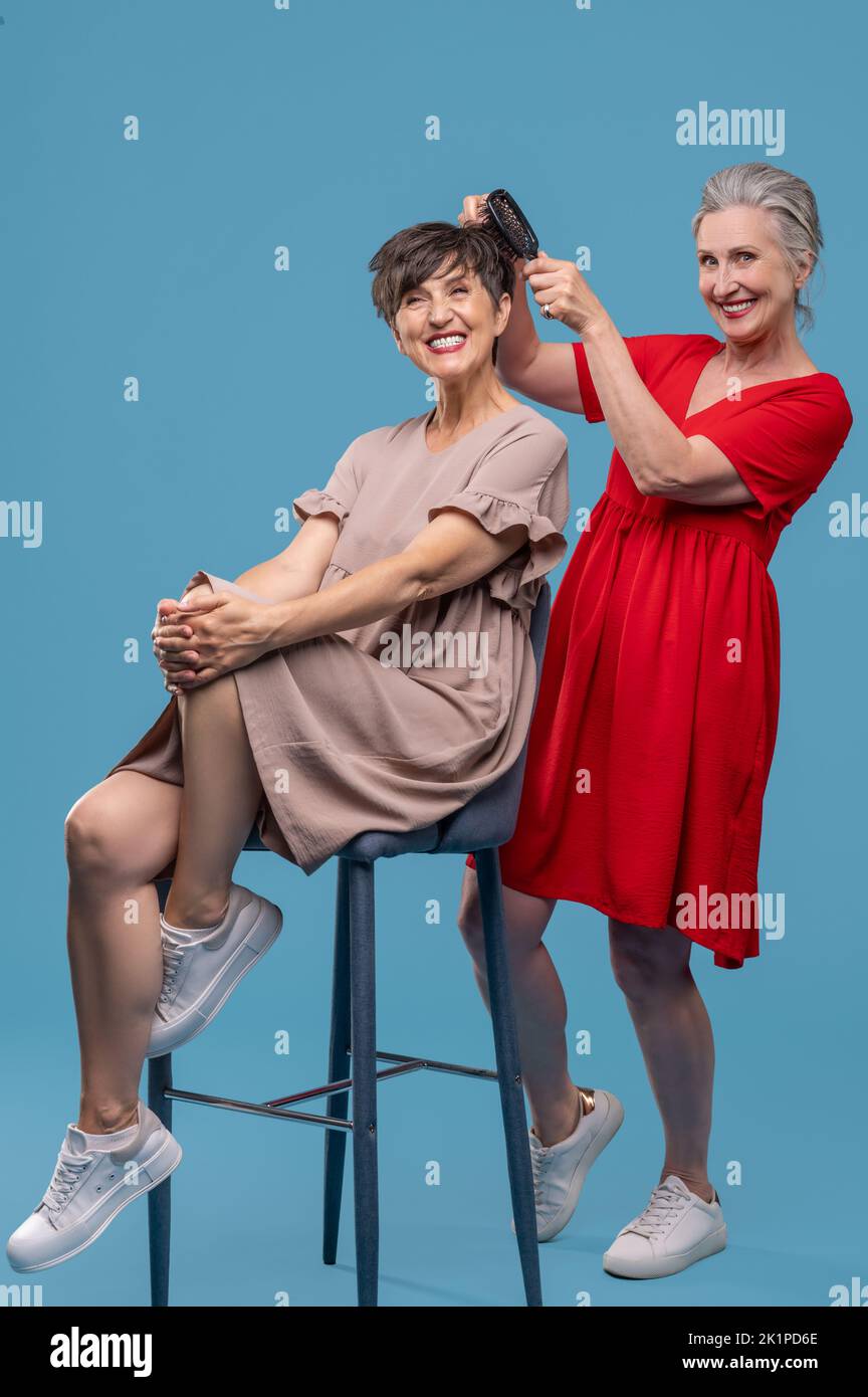 Woman in red dress making her friends hair and looking excited Stock Photo
